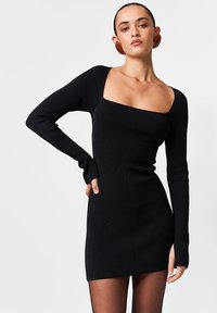 Fekete bordázott miniruha hosszú ujjakkal, négyzet alakú nyakkivágással és testhez simuló sziluettel. Sima textúrájú, varrásokkal díszített felsőrésszel.