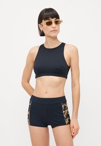 Black sports bra and black shorts with a patterned side panel in shades of brown, pink, and cream. Made of stretchy, smooth fabric.