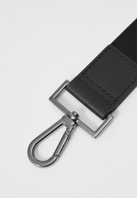 Sort stofrem med en struktureret overflade, der har en sølvfarvet metalklips til fastgørelse. Klipset har en afrundet krogform.
