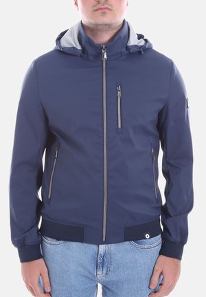 Uomo che indossa una giacca con cappuccio blu navy con tasche con cerniera e jeans azzurri, ritagliato al collo e alla vita.