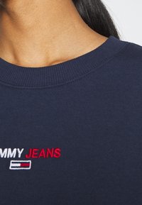 Mörkblå sweatshirt med ribbat halsband, där "TOMMY JEANS" är broderat i vitt och rött. Mjuk bomullstyg med en avslappnad passform.