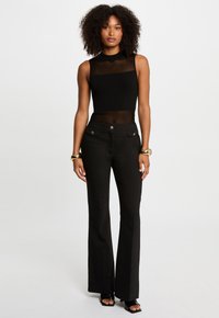 Top noir sans manches avec texture côtelée, col montant ; pantalon noir évasé avec des boutons à la taille, tissu lisse, légère brillance.