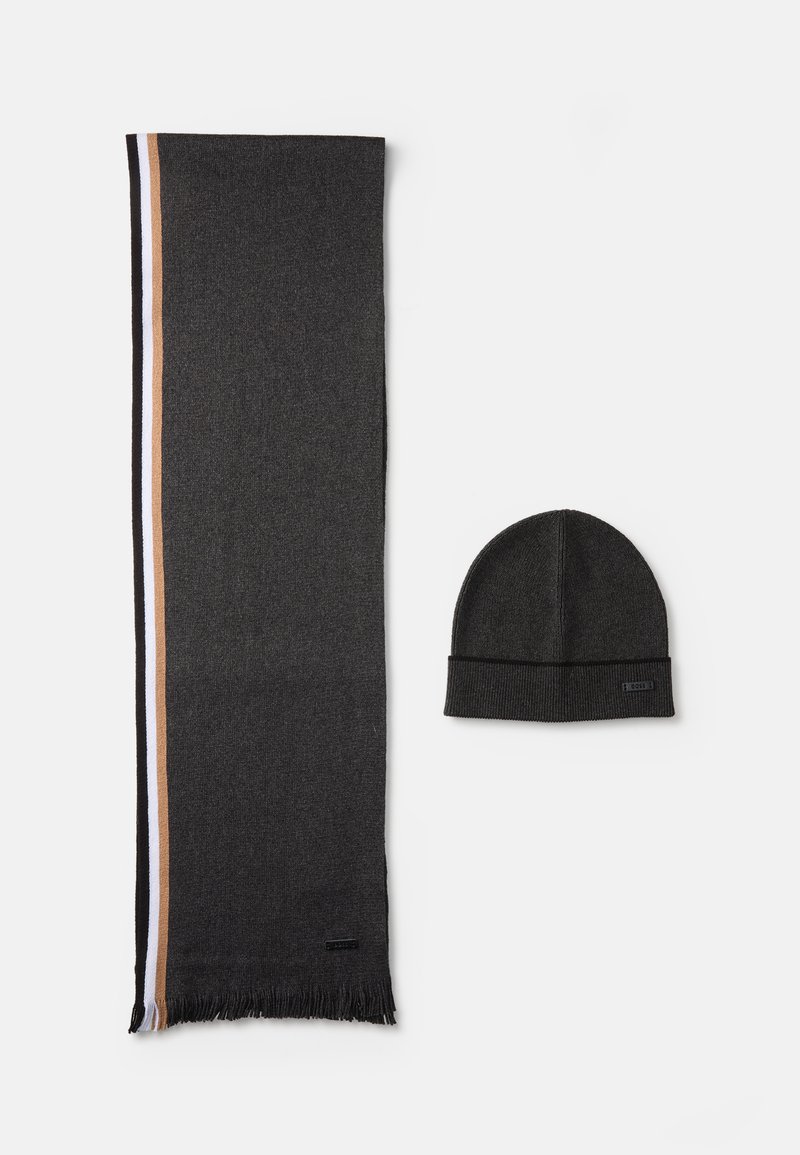 Cachecol preto com franjas nas bordas, apresentando uma faixa lateral em bege e branco, acompanhado de um gorro preto combinando. Ambos são em tecido de malha.