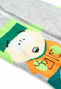 Calzini grigi con un personaggio dei cartoni animati che indossa un cappello verde e una maglietta arancione. Il design include grandi occhi bianchi e dettagli verdi.