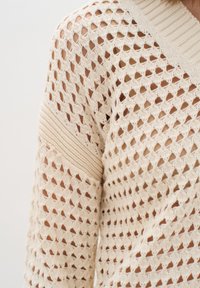 Strickpullover in cremefarbe mit einem lockeren offenen Strickmuster, gerippten Akzenten an den Schultern und einem V-Ausschnitt. Strukturierter, leichter Stoff.