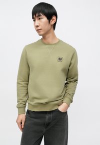 Khakigrønn genser med rund hals, ribbestrikkede mansjetter og kant; har en liten logopatch på brystet og en jevn tekstur.