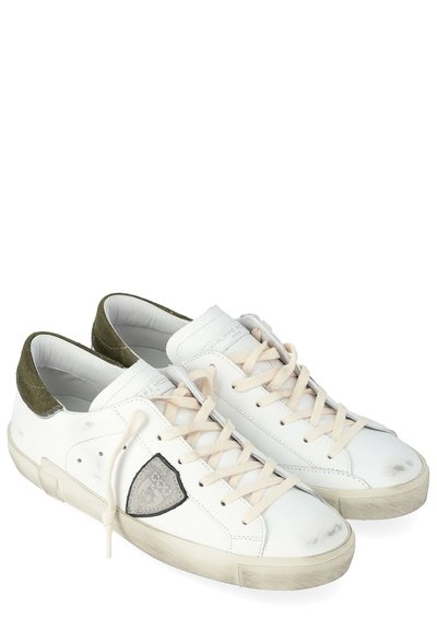 Zapatillas blancas de cuero con un parche de logo gris texturizado, cordones beige claro y detalles en ante verde en el talón. Pequeñas marcas de desgaste en la puntera.