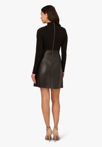 Schwarzes Langarmoberteil mit hohem Kragen, kombiniert mit einem figurbetonten Lederrock. Verfügt über einen Reißverschluss auf der Rückseite und eine glatte, elegante Textur.
