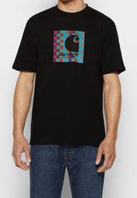 Camiseta de algodón negra con un colorido diseño abstracto de tablero de ajedrez y un logo circular en el centro. Mangas cortas, corte relajado.