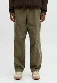 Pantaloni larghi color verde oliva realizzati in morbido cotone, con una vestibilità rilassata, tasche laterali e una finitura leggermente testurizzata, abbinati a sneakers beige.