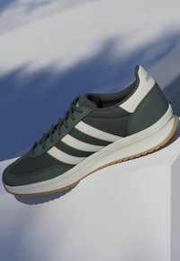 Baskets Adidas gris foncé et blanc avec semelle en gomme reposant sur une surface blanche sur fond bleu ombré.