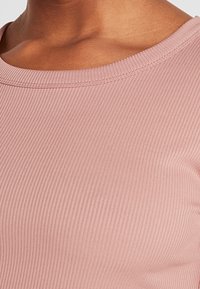 Top de tejido acanalado en rosa claro con cuello redondo y detalles de textura visibles, mostrando un primer plano de la zona del cuello y el hombro.