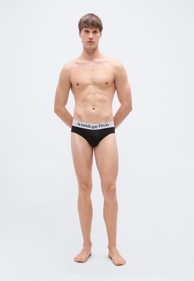 Μαύρα βαμβακερά εσώρουχα με λευκή μέση που φέρει το κείμενο «Sounds gay I’m in.» Ο σχεδιασμός είναι μινιμαλιστικός και εφαρμοστός.