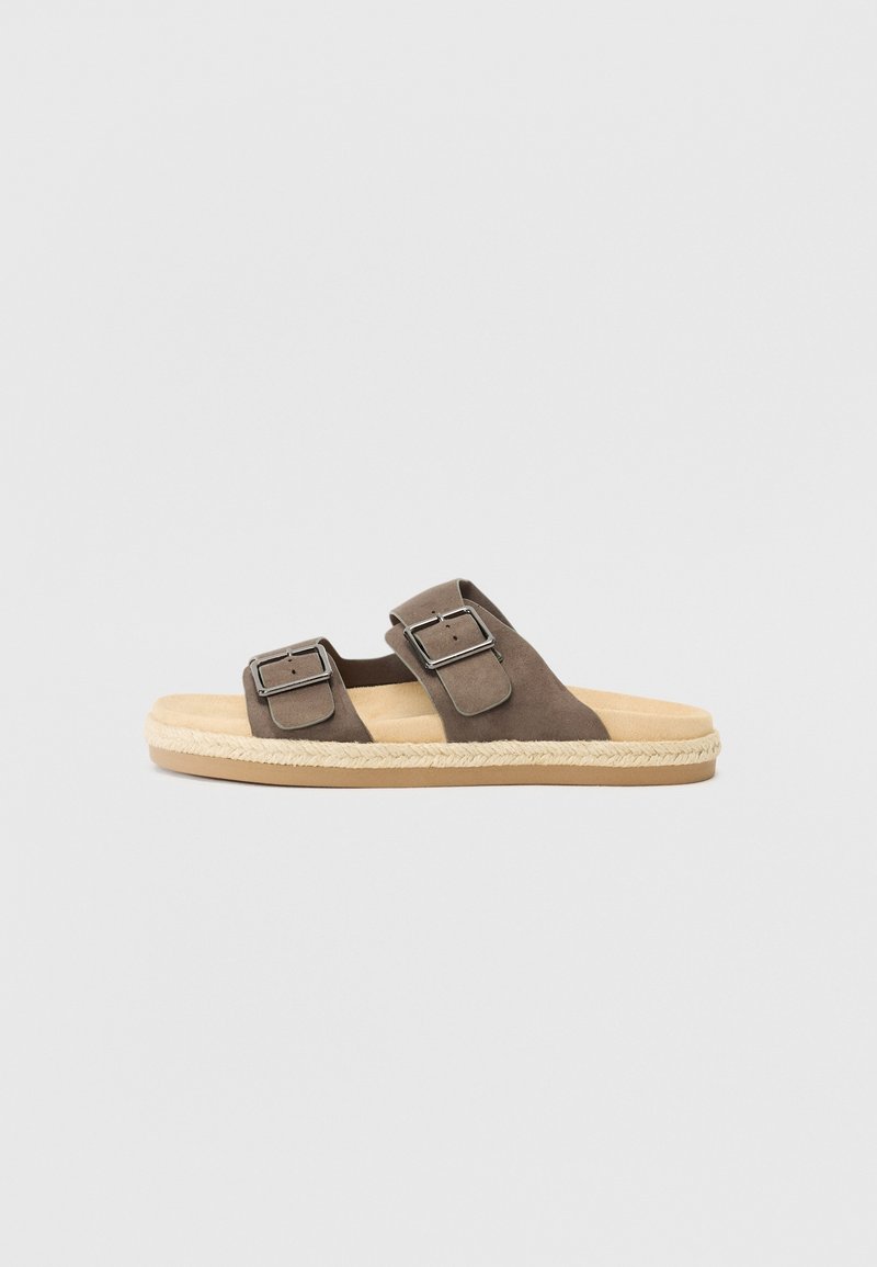 Sandale à enfiler en daim marron avec deux brides réglables à boucle et une semelle beige coussinée sur fond blanc.