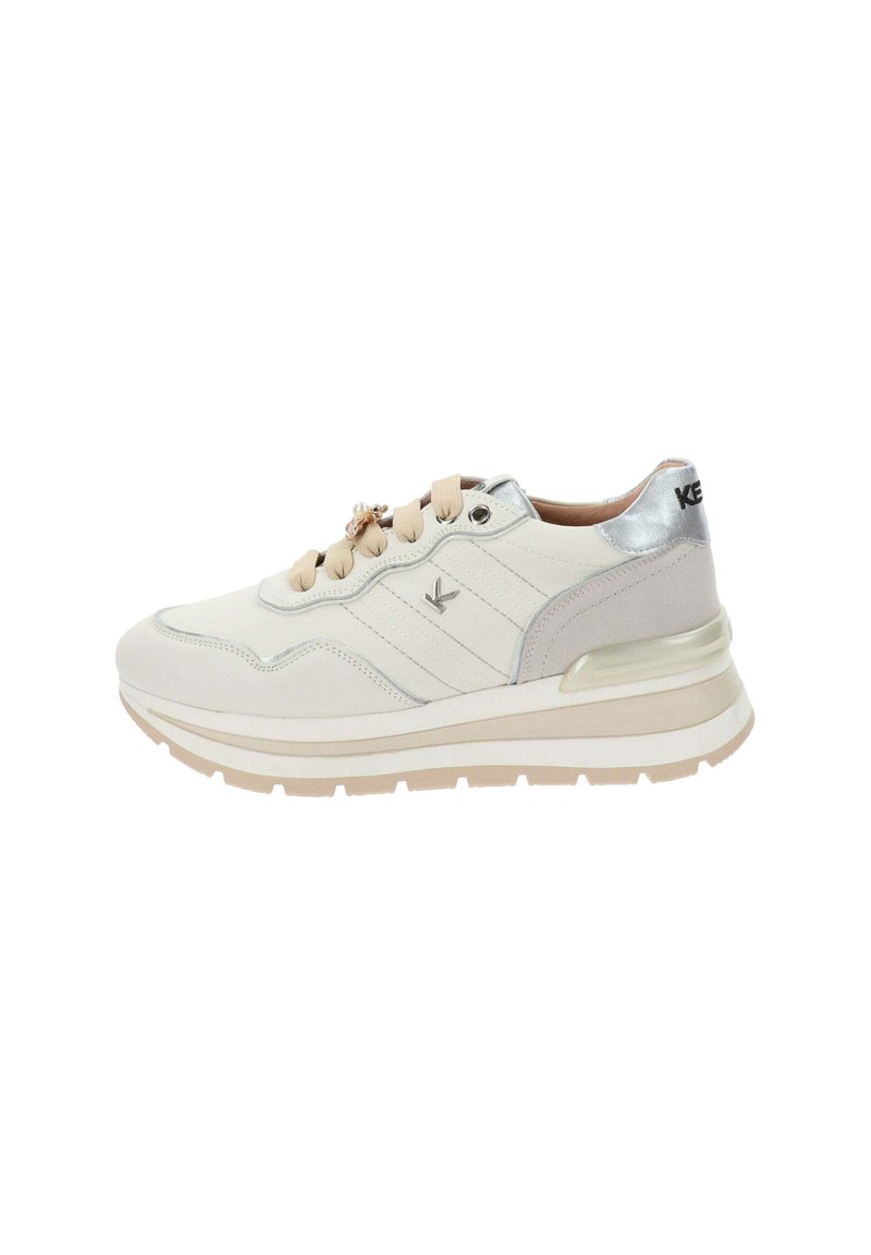 Sneaker bianco e beige con suola chunky, linguetta sul tallone in argento metallizzato, lacci beige e piccolo charm decorativo sui lacci, logo laterale visibile.