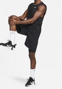 Top deportivo negro sin mangas y pantalones cortos, combinados con zapatillas de correr en blanco y negro y calcetines blancos con un logo. Tela suave y ligera.