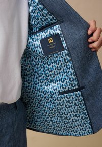 Giacca da abito blu scuro con foderatura geometrica blu chiaro, dotata di taschino sul petto e un'etichetta del marchio cucita all'interno.