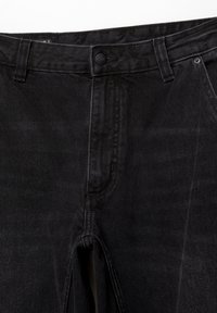 Vaqueros negros de mezclilla con corte recto, cierre de botón, trabillas para cinturón y una textura sutil. Sin patrones ni detalles visibles.