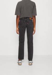 Jeans de mezclilla negros con corte recto, con bolsillos traseros y una etiqueta de piel marrón. Combinados con zapatillas negras y blancas.