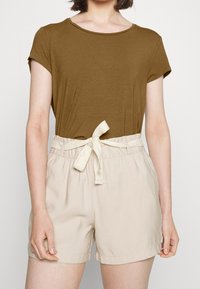 Krátký rukáv hnědý top a béžové šortky s páskem na stažení v pase. Šortky mají hladkou strukturu a ohrnuté okraje.