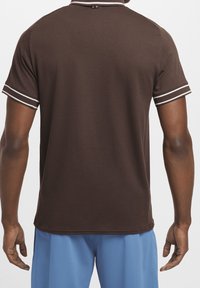 Brun polo skjorta med en texturerad tyg, vit kant vid kragen och ärmarna, korta ärmar och en nederkant som ligger precis ovanför midjan.