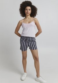 Débardeur rose clair avec bordure en dentelle, associé à un short rayé bleu marine et blanc. Le modèle porte des baskets blanches, illustrant une tenue décontractée d'été.