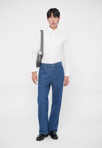 Traperice s plavim uzorkom, u kombinaciji s bijelom košuljom dugih rukava. Outfit se ističe ravnim prednjim dijelom i modernim krojem.