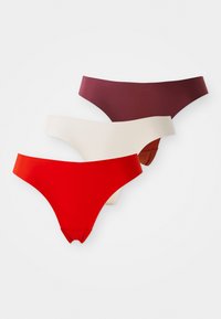 Drie naadloze stringonderbroeken gestapeld, gekleurd in rood, beige en donker bordeaux, op een effen witte achtergrond.