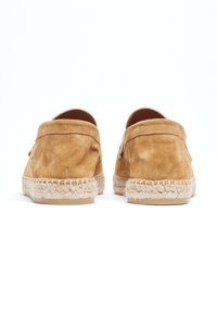 Espadrilles de ante en color marrón con una textura suave, forma redondeada y suela de cuerda de yute. Presentan un diseño sin cordones sin hardware visible.