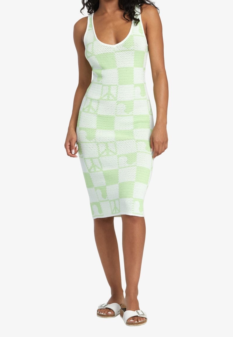 Abito a maglia a scacchi verde e bianco con forma attillata, scollatura a barchetta e tessuto testurizzato. Indossato con sandali piatti bianchi.