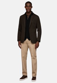 Brown wool blazer over a black zippered sweater, paired with beige pants and brown suede sneakers. Simple and tailored design.