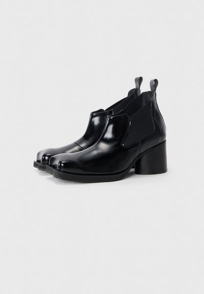 Black glossy ankle boots with elastic side panels, round toe, and a block heel. Textured black fabric accents on the sides.