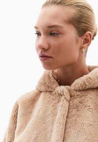 Kabát z umělé kožešiny v světlé béžové barvě s kapucí, který má jemnou strukturu a uzavírání na uzel u límce.