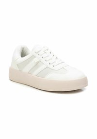 Zapatillas deportivas blancas con parte superior de cuero sintético, que destacan acentos y cordones de textil gris claro. Suela de goma gruesa y texturizada.