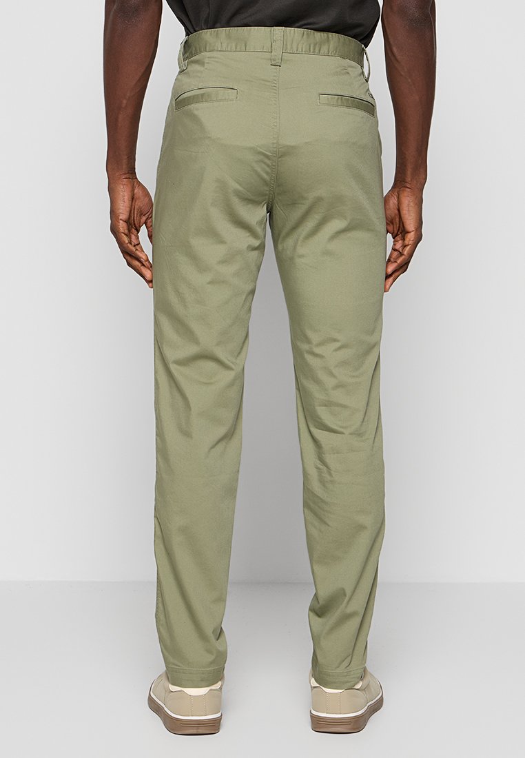 Khaki broek met een slim fit, gladde stof, twee achterzakken en een elastische tailleband, gecombineerd met beige schoenen.