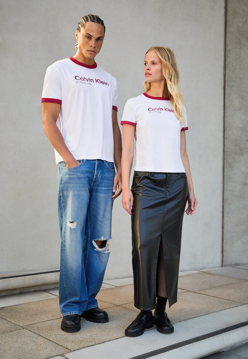 Dvi modeliai vilki atitinkančius baltus marškinėlius su raudonu apvadu, ant kurių užrašas "Calvin Klein". Viena jų derina marškinėlius su suplyšusiais mėlyniais džinsais, o kita - su juoda odine sijoną.
