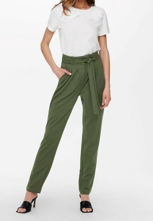 Femme portant un haut blanc à manches courtes avec un col festonné et un pantalon taille haute vert olive avec ceinture nouée, associé à des sandales noires à talons.