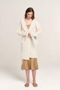 Weiße Strickjacke mit langen Ärmeln und Bindebandverschluss, getragen über einem seidigen beigen Kleid. Weiche Textur und lockere Passform. Leichtes Design.