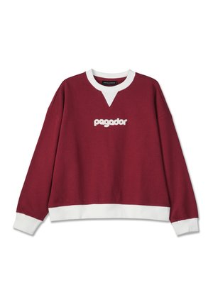 Burgundi pulóver fehér részletekkel, V nyakú kialakítással, és fehér hímzett "pegador" logóval a mellkason.