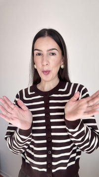 Frau in einem braun-weiß gestreiften Pullover klatscht mit gespitzten Lippen vor einem schlichten hellen Hintergrund.