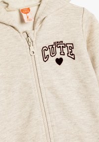 Sudadera con capucha beige para bebé con cremallera frontal, texto "SIEMPRE BONITO" y gráfico de corazón en el pecho, etiquetada para 9-12 meses, tamaño 76-80 cm.