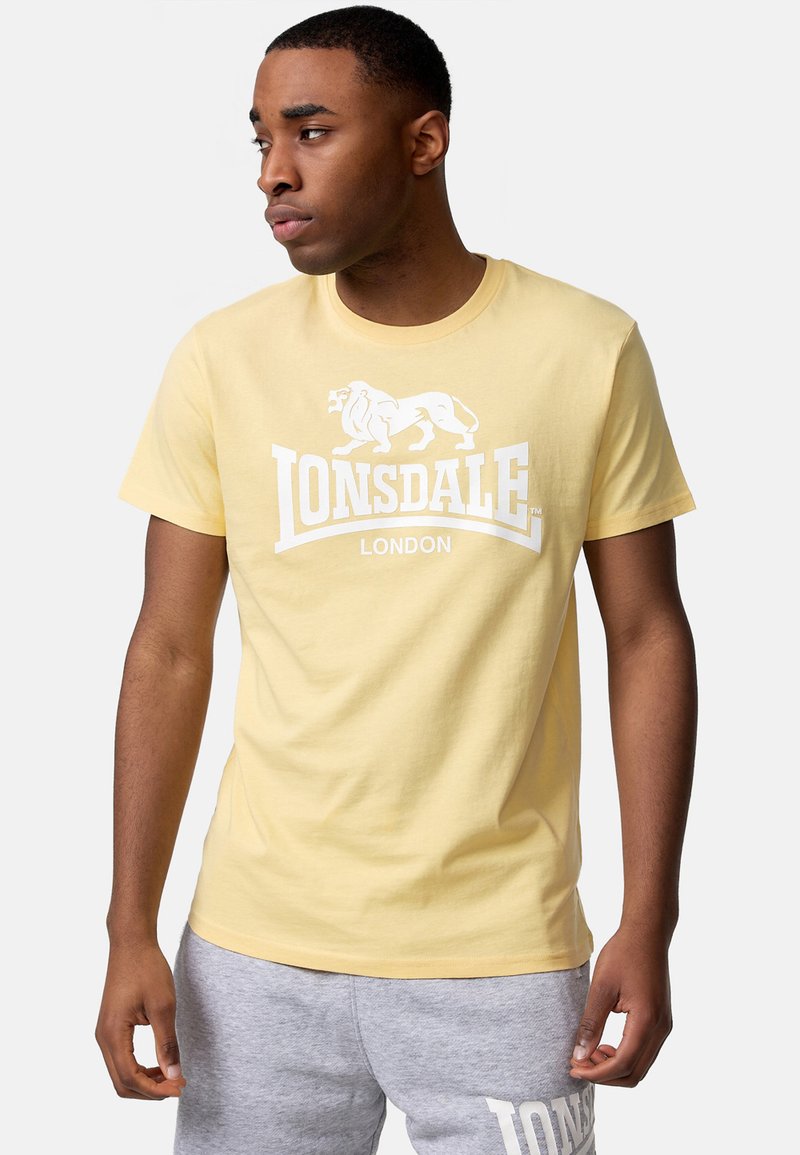 Geltonas medvilnės marškinėliai su baltu liūto grafiku ir "LONSDALE LONDON" tekstu. Trumpomis rankovėmis, apvaliu kaklu, laisvas kirpimas.