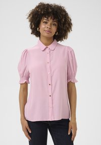 Ružový krátky rukáv blúzka s golierom, dekoratívnymi gombíkmi na prednej strane a elastickými nadýchanými rukávmi. Hladká tkanina s jemným leskom.