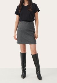 T-shirt noir associé à une jupe écossaise de longueur genou. Le mannequin porte des bottes noires jusqu'aux genoux. Design simple et ajusté avec une texture lisse.