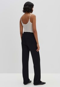 Zwarte wijde broek van soepel materiaal, met twee achterzakken en een getailleerde pasvorm, gedragen met een lichtgrijs tanktop.