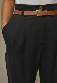 Crne hlače s glatkom teksturom i opuštenim krojem, s bočnim džepovima i smešnim kožnim remenom s metalnom kopčom.