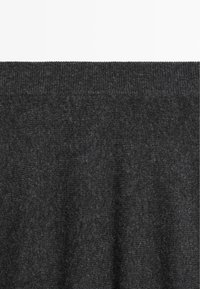 Donkergrijze gebreide stof met een gladde textuur en een geribbelde rand. Het materiaal lijkt zacht en warm, geschikt voor bovenkleding of voor laagjes.