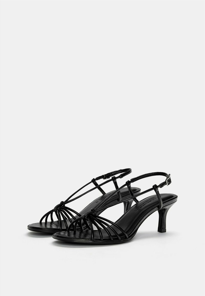 Sandalias negras con tiras y tacón delgado. Fabricadas en material sintético suave, con un diseño entrecruzado y correa en el tobillo ajustable.