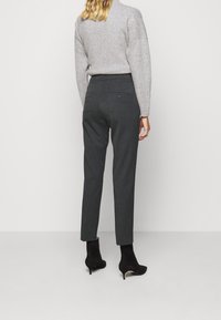 Pull gris, pantalon gris foncé sur mesure, coupe slim, poches arrière avec boutons, associé à des bottines noires, texture de tissu lisse.