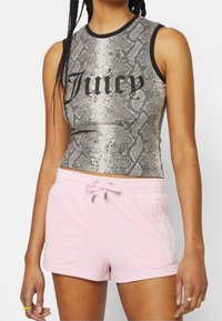 Femme portant un crop top gris sans manches à imprimé serpent avec le texte « Juicy » et un short à cordon rose clair.
